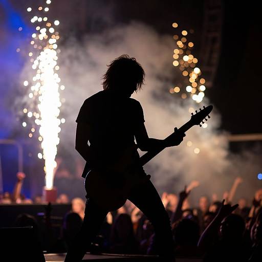 Silhouetted rock guitarist with messy hair, playing electric guitar, against vibrant stage lights and fog, with an energetic crowd in the background. Phot