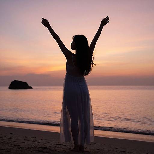 Silhouetted woman with arms raised in a flowing dress stands on a beach at sunset, with a rocky island in the background.