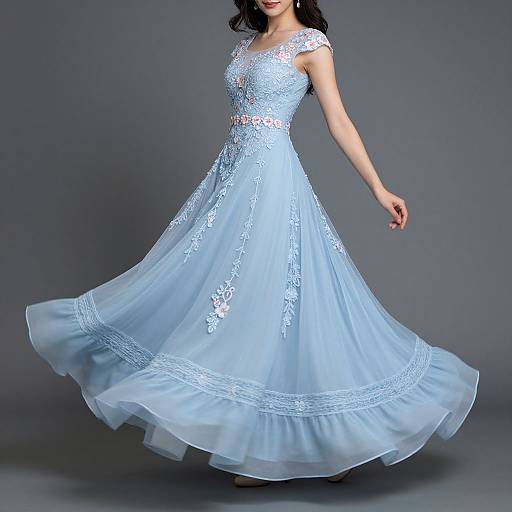 Photograph of a woman in a light blue, lace-embellished, full-length, A-line dress with a sheer, layered skirt, standing