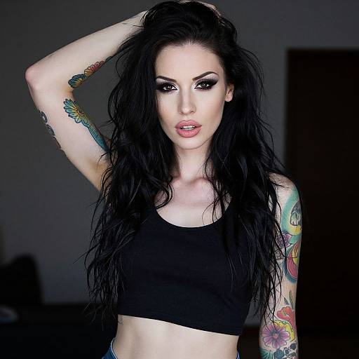 Photograph of a pale-skinned woman with long black hair, wearing a black sports bra, revealing colorful tattoos on her arms, against a dark background