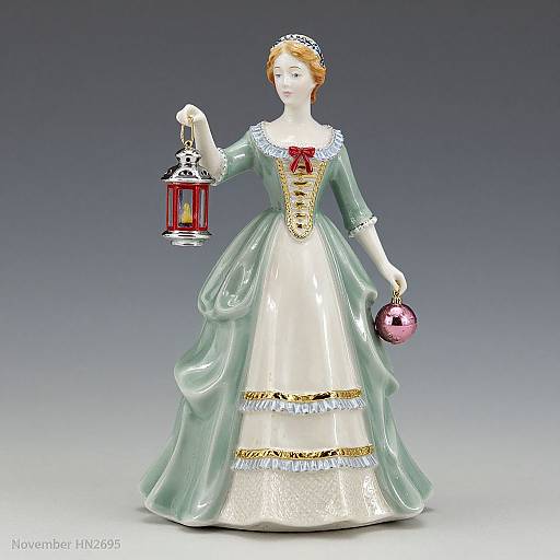 Photograph of a porcelain doll with red hair, wearing a green and white Victorian-style dress, holding a red lantern and pink ornament, against a gray