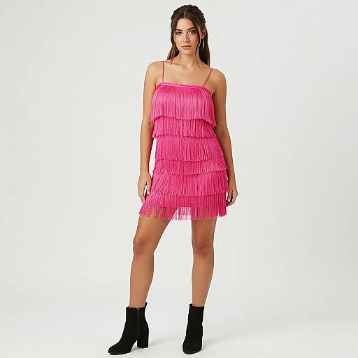 Photograph of a young woman with long brown hair, wearing a bright pink, ruffled, spaghetti-strap mini dress and black ankle boots, standing