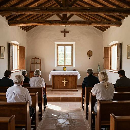 Photograph of a small, rustic church with white walls, wooden ceiling beams, and tiled floor. Six elderly churchgoers, four men and two