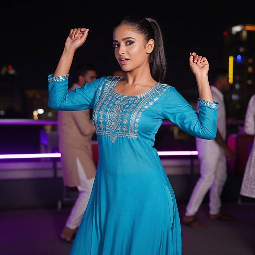 Photograph of a beautiful woman with dark hair in a ponytail, wearing a vibrant blue traditional dress with intricate embroidery, posing confidently with hands up,