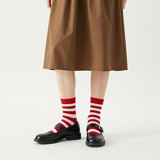 Photograph of a child's lower body in a brown skirt, black shoes, and red-and-white striped socks, standing against a white background.