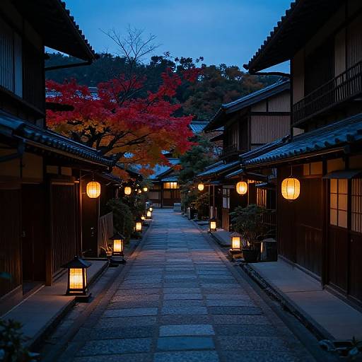 Photograph of a tranquil Japanese alley at dusk, illuminated by warm lanterns, with red autumn leaves in the background.