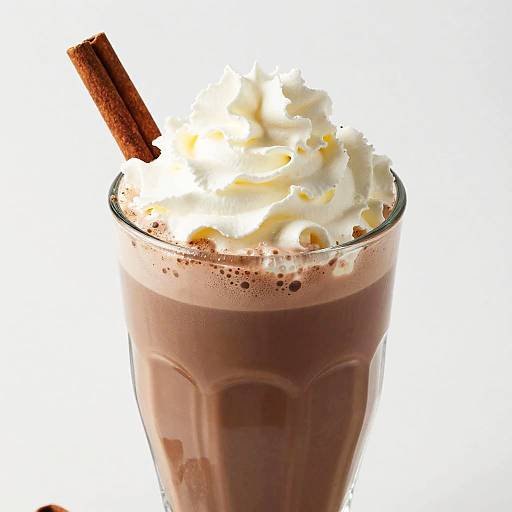 Photograph of a glass of rich chocolate milkshake topped with fluffy whipped cream and a cinnamon stick, against a white background.