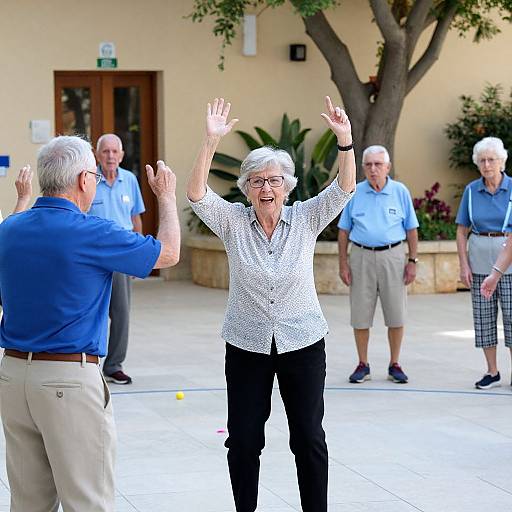 Photograph of elderly woman with short white hair, wearing white polka-dot blouse and black pants, joyfully raising arms, surrounded by elderly men and