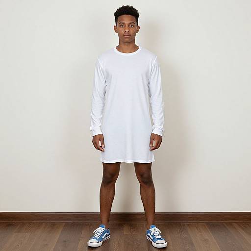 Photograph of a young Black man with short, curly hair, wearing a white long-sleeve shirt and shorts, blue sneakers, standing against a