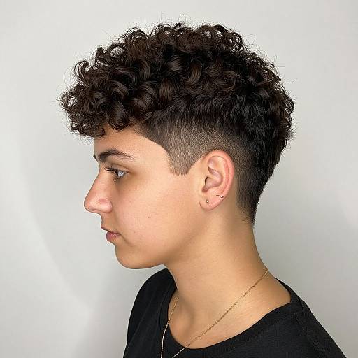 Photograph of a young man with short, curly black hair, side profile, light skin, black shirt, gold necklace, white background.