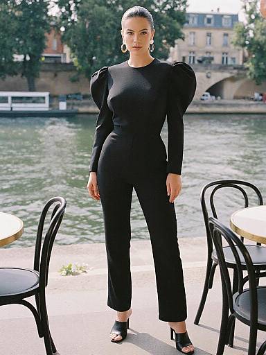 Photograph of a tall, slim woman with dark hair in a sleek updo, wearing a black, long-sleeve, high-waisted
