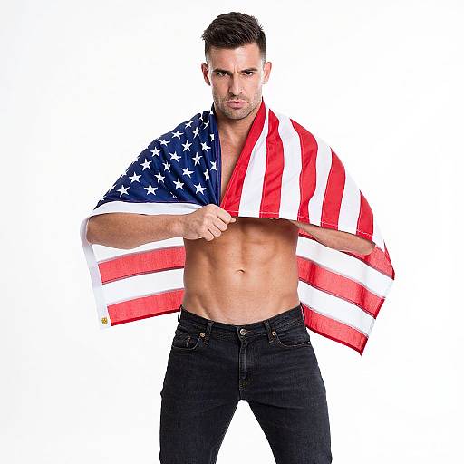 Photograph of a muscular, fair-skinned man with short dark hair, mustache, and blue eyes, wearing black jeans, draped in an American