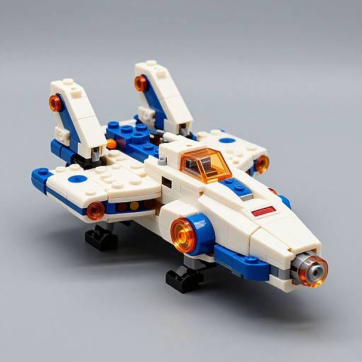 Photograph of a colorful LEGO space fighter with white, blue, and orange elements, featuring two orange engines, a cockpit, and twin vertical stabilizers