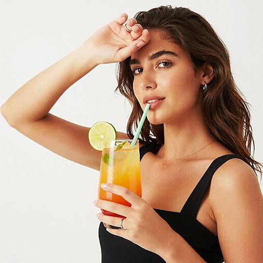 Photograph of a young woman with long brown hair, wearing a black tank top, sipping a colorful cocktail with a lime slice, white straw,