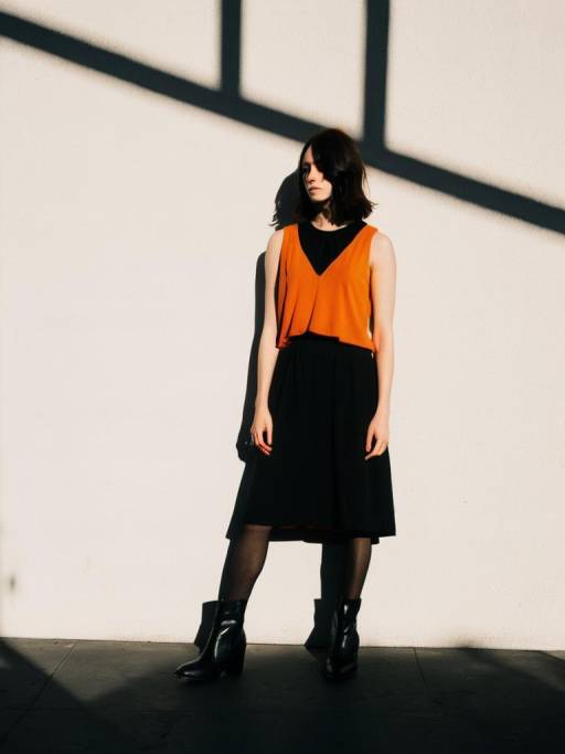 Woman in Orange and Black Outfit against White Wall