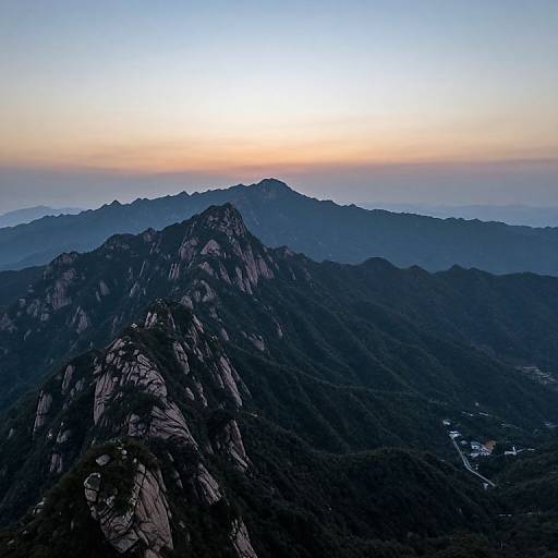 Photograph of a mountainous landscape at sunrise, with dark, rocky peaks in the foreground and a gradient sky from orange to blue in the background.