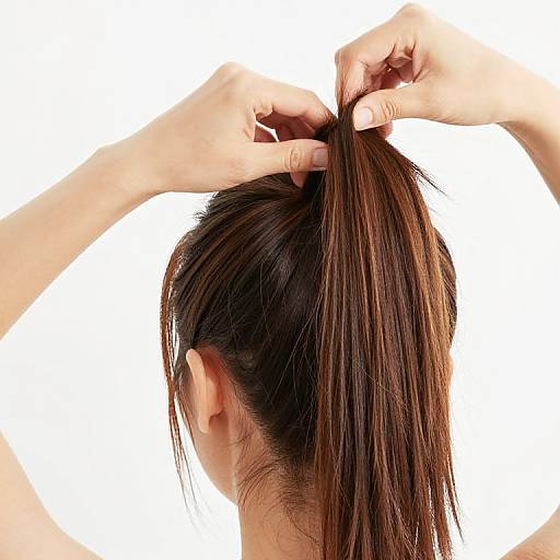 Photograph of a person with light skin, dark brown hair, and a slender build, using both hands to tie their long hair into a ponytail