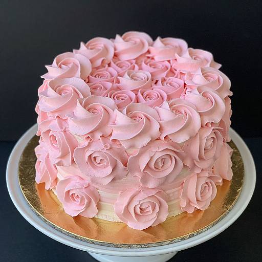 Photograph of a pink rose-piped cake with intricate rosettes, on a gold-trimmed white cake stand, against a black background.