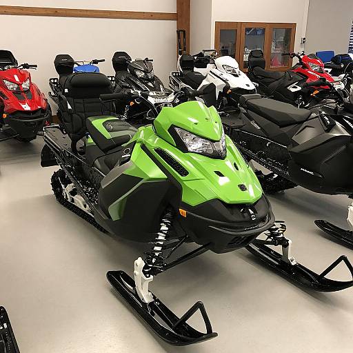 Photograph of a showroom featuring multiple snowmobiles, with a green and black front-facing snowmobile in the foreground, surrounded by red, blue,