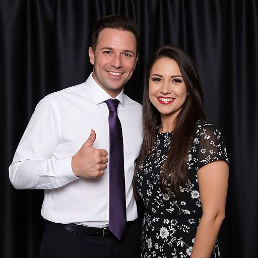 Photograph of a smiling white man with dark hair in a white shirt and black tie, giving a thumbs-up, beside a smiling woman with long dark