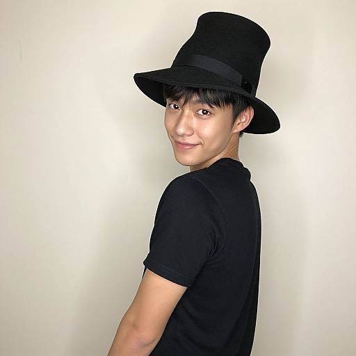 Photograph of a smiling Asian man with fair skin, wearing a black top hat and black t-shirt, turned slightly to the side against a plain white