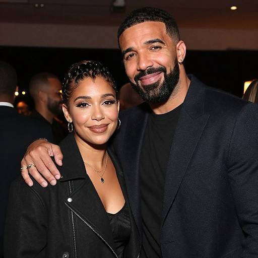 Photograph of a smiling, bearded Black man in a black blazer and black shirt, standing close to a beautiful Black woman with braided hair