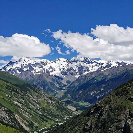 Photograph of a vibrant mountain landscape with snow-capped peaks, lush green valleys, and a bright blue sky with fluffy white clouds.
