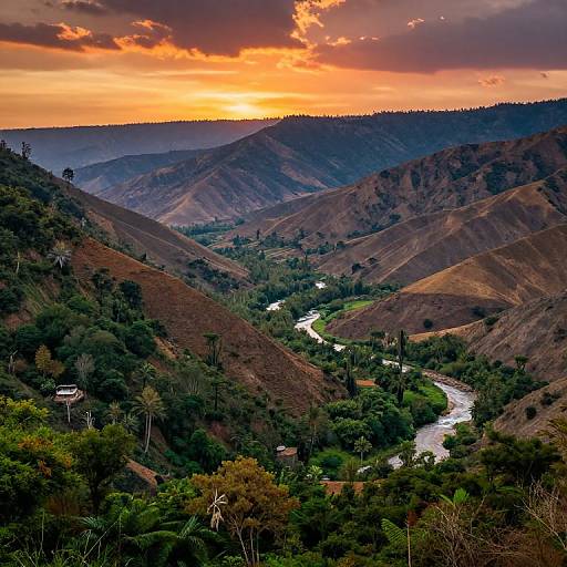Photograph of a stunning sunset over a lush, green valley with a winding river, surrounded by rolling brown hills and dense forests. Orange and purple clouds