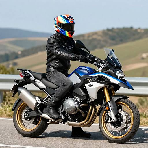 Photograph of a motorcyclist in black leather gear and colorful helmet, riding a blue and white Honda sport bike on a sunny, hilly road
