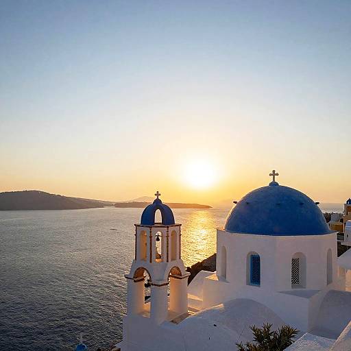 Photograph of a Greek island sunset, featuring a white-washed church with blue domes and bells, overlooking a calm, golden-hued sea.