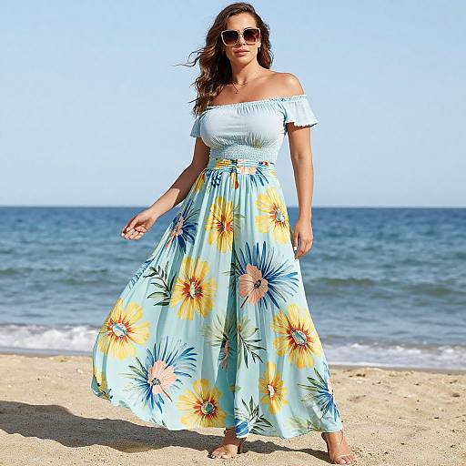 Photograph of a woman with wavy brown hair, wearing off-shoulder white top and sunflower-patterned floral dress, standing on sunny beach