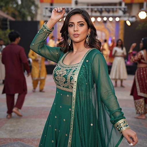 Photograph of an attractive Indian woman in a green, embroidered traditional lehenga, with gold jewelry, posing confidently at a lively outdoor event. Blurred