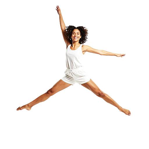 Photograph of a joyful, curly-haired woman in a white dress, mid-jump with arms and legs spread wide, against a white background.