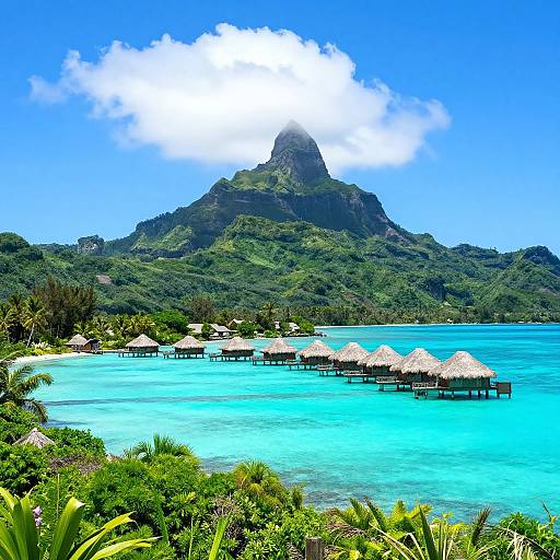 Photograph of a tropical island with turquoise waters, thatched-roof overwater huts, and a lush green mountain peak under a bright blue sky