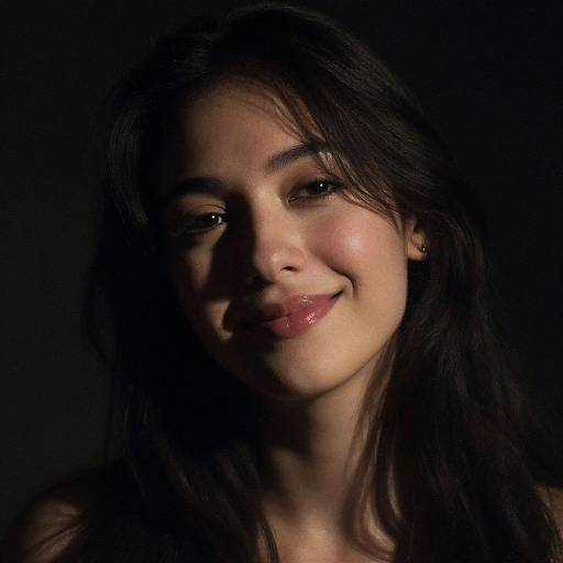 Photograph of a young woman with long dark hair, soft smile, and glossy lips, illuminated against a dark background.