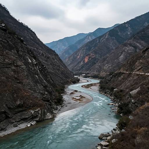 Photograph of a narrow, turquoise river winding through a rugged, mountainous valley with steep, forested slopes under a cloudy sky.