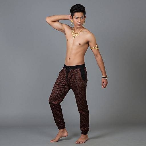 Photograph of a young, shirtless Asian man with short black hair, wearing black checkered pants, gold armlets, and bracelets, standing bare