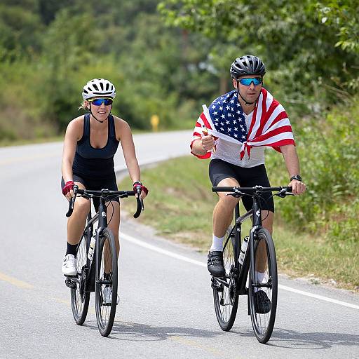 Photograph of two cyclists on a road: a woman in a black tank top and helmet, and a man wearing an American flag shirt and reflective sunglasses