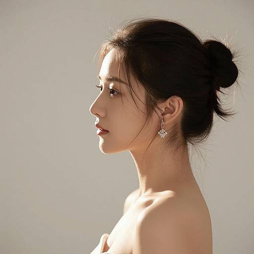 Photograph of a young Asian woman in profile, sunlit, with dark hair in a bun, wearing delicate earrings, and bare shoulders.