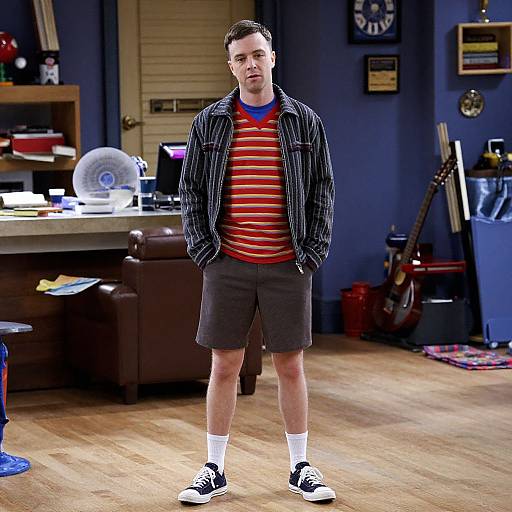 Photograph of a young man with short brown hair, wearing a striped jacket, red and yellow striped shirt, black shorts, white socks, and black