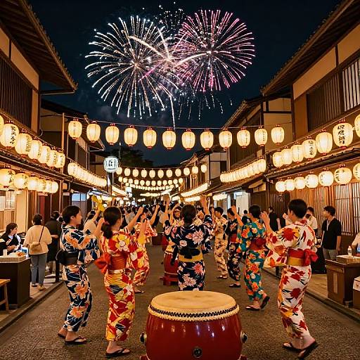 Nighttime photograph of a vibrant Japanese festival. Dancers in colorful kimonos perform near a drum in a lantern-lit alley, with colorful fireworks