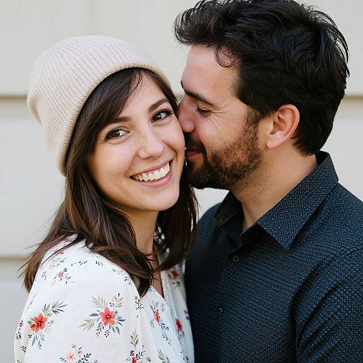 Photograph of a smiling couple; woman with white beanie, floral shirt, and dark brown hair, man with black shirt, dark hair, and