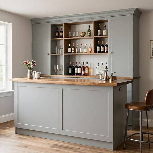 Modern kitchen bar with gray cabinets, wooden countertop, assorted liquor bottles, glasses, vase with flowers, and a brown bar stool. Bright, natural