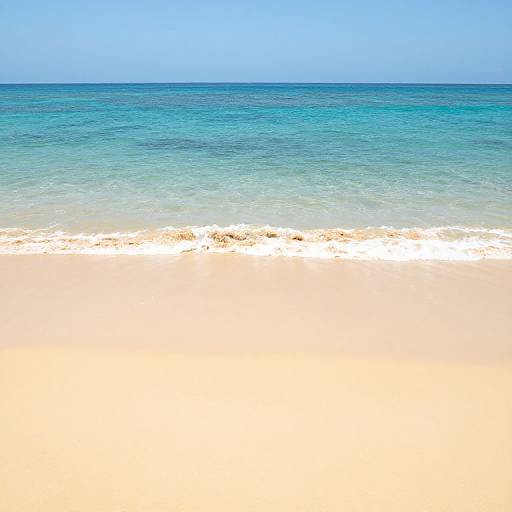 Photograph of a serene beach with clear, turquoise ocean waves gently touching white, sandy shore under a bright blue sky.