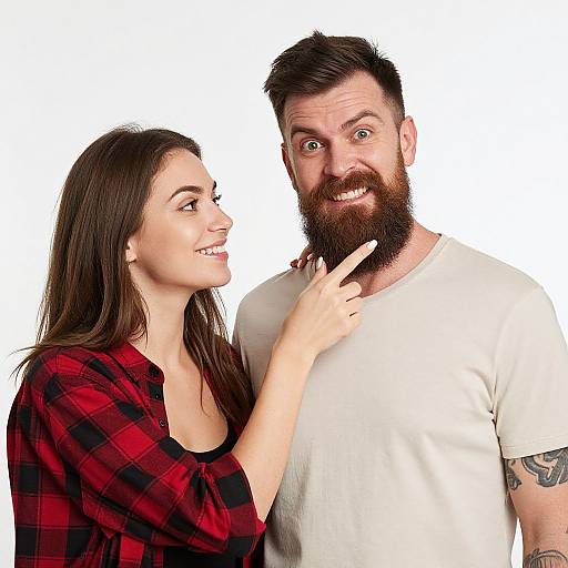 Photograph of a smiling woman with long brown hair in a red plaid shirt playfully pointing at a surprised bearded man in a white t-shirt