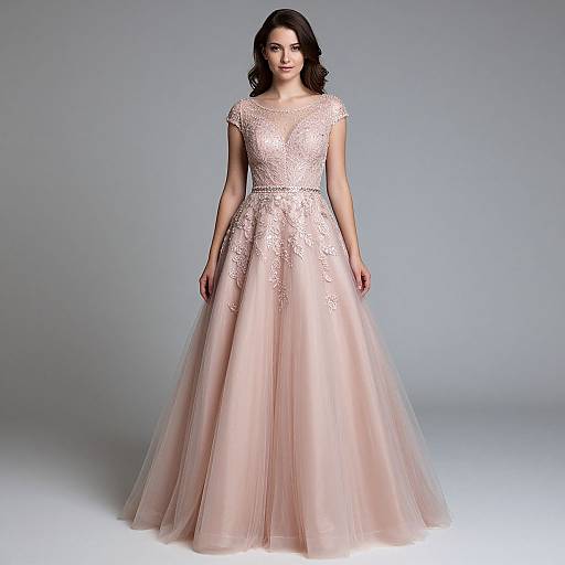 Photograph of a dark-haired woman in an elegant, sheer-embellished, pink ball gown with a full skirt, standing against a gray background