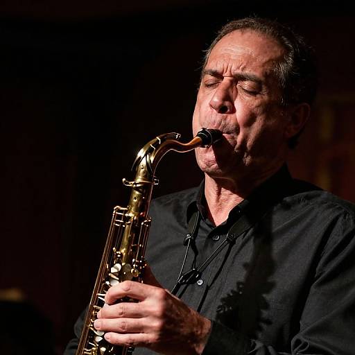 Middle-aged man with short dark hair, black shirt, and mustache passionately playing a golden saxophone on stage, illuminated by spotlight.