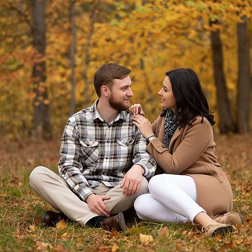 Photograph of a couple sitting on grass in an autumn forest, with vibrant yellow leaves; the man in plaid shirt and beige pants, the woman