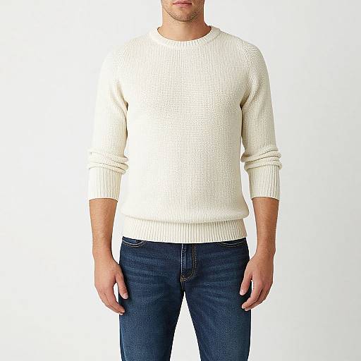 Photograph of a man with light skin, wearing a white, textured knit sweater and dark blue jeans, standing against a plain white background.
