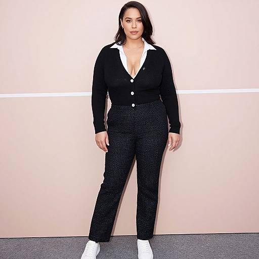 Photograph of a plus-sized woman with medium-length black hair, wearing a black cardigan with white collar, black pants, and white sneakers, standing